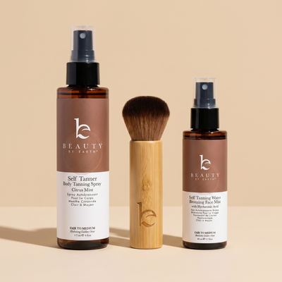 Two bottles of 'Beauty by Earth' self-tanner and a kabuki brush on a beige background