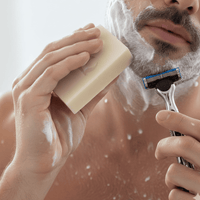 Man shaving with a razor and soap, with a blurred background