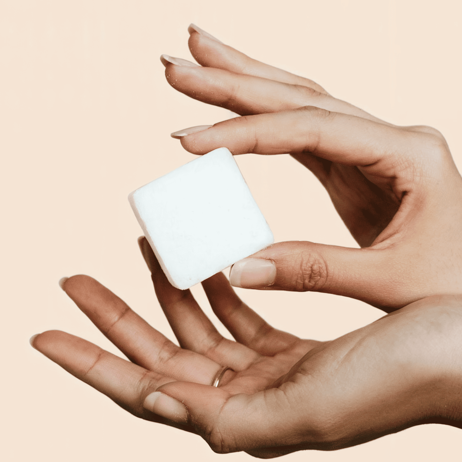 Hand holding a small white cube against a beige background