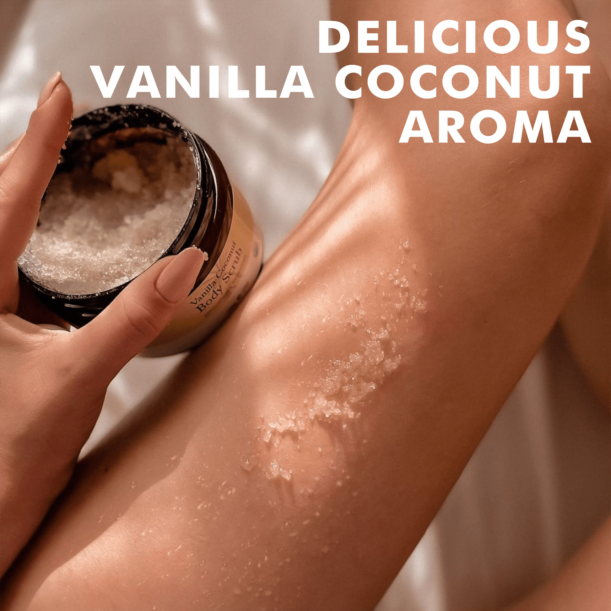 Person applying a scrub from a jar to their leg with text 'Delicious Vanilla Coconut Aroma'.