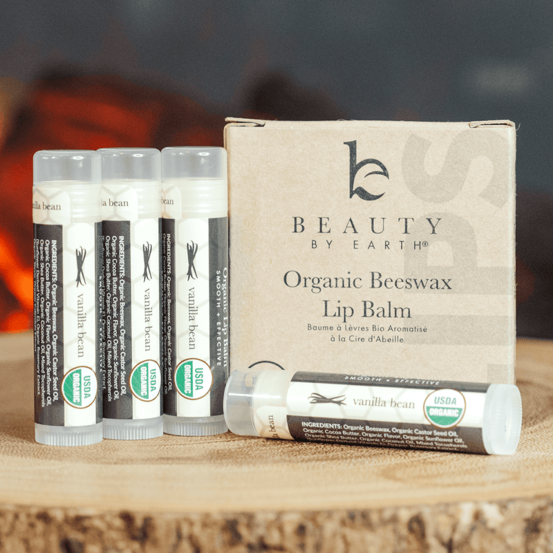 Set of Beauty by Earth organic beeswax lip balms on a wooden surface with a blurred background.