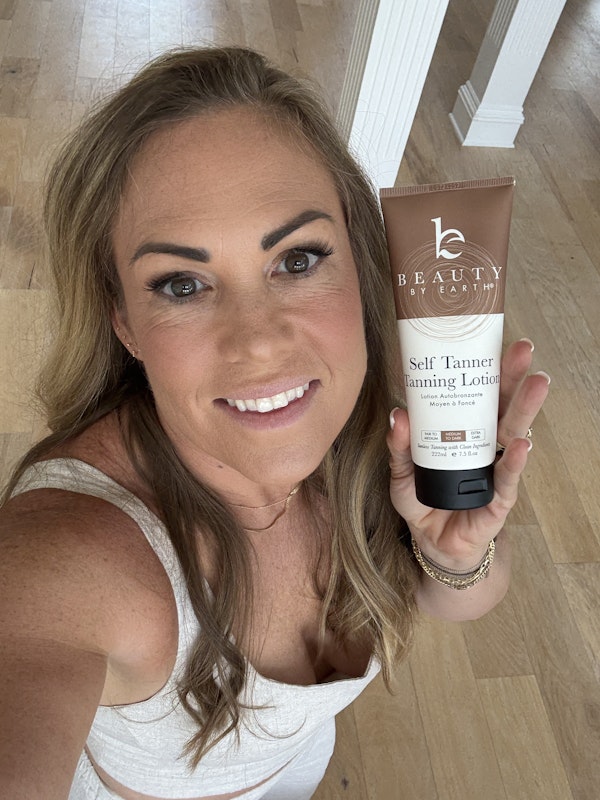 Prudence holding a tube of 'Beauty by Earth' self-tanner in a home setting.