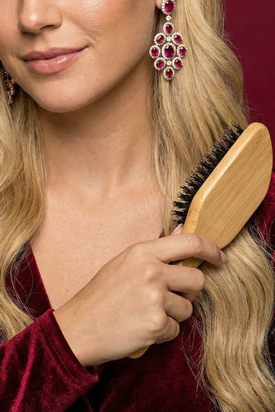 Woman brushing her hair with a wooden brush against a red background