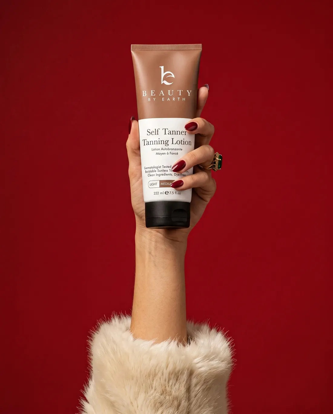A hand holding Self Tanner Body Lotion against a deep red backdrop